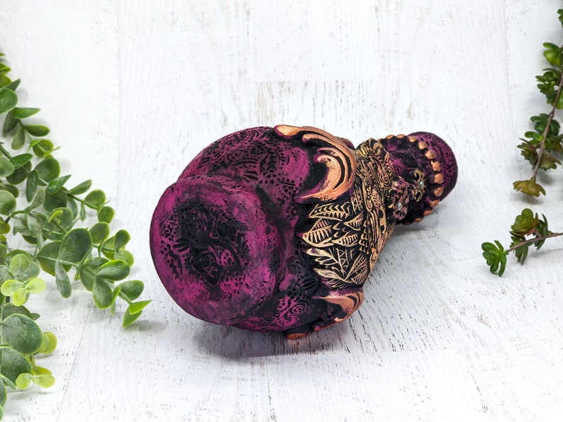 May include: A pink and gold ceramic vase with intricate floral designs. The vase is decorated with gold accents and has a textured surface.