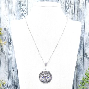 May include: A silver necklace with a round pendant featuring a detailed tree of life design with blue and purple gemstones.