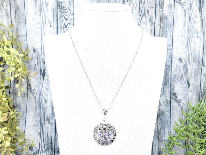 May include: A silver necklace with a round pendant featuring a detailed tree of life design with blue and purple gemstones.