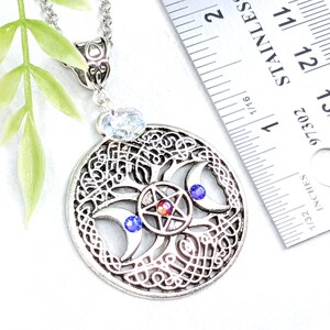 May include: Silver pendant necklace featuring a tree of life design with a triple moon and pentagram. The pendant is approximately 1 3/4 inches in diameter and has blue and red crystals.