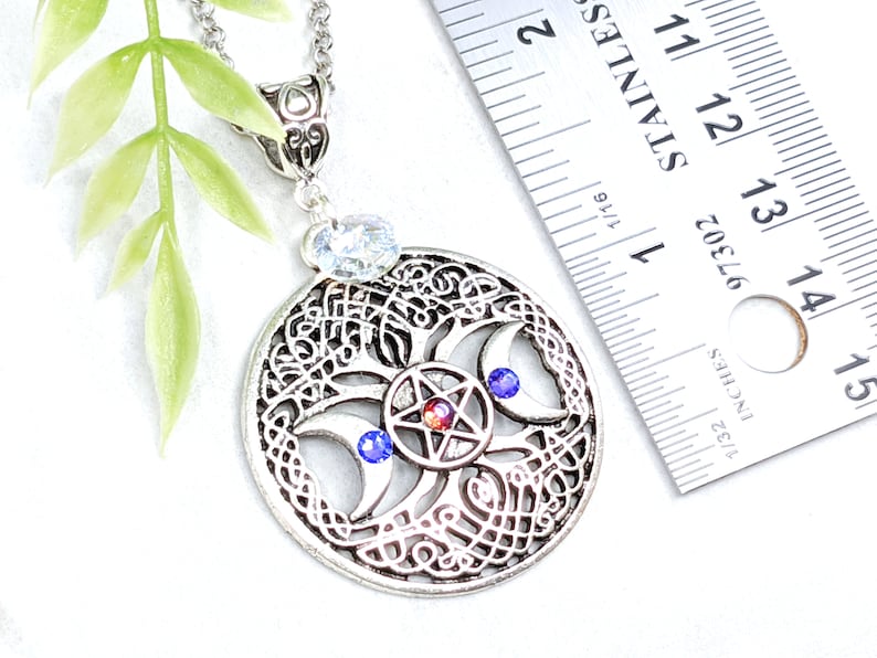 May include: Silver pendant necklace featuring a tree of life design with a triple moon and pentagram. The pendant is approximately 1 3/4 inches in diameter and has blue and red crystals.