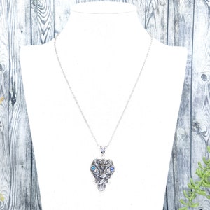May include: A silver necklace with a detailed owl pendant featuring blue eyes. The owl pendant is a heart shape with intricate details.