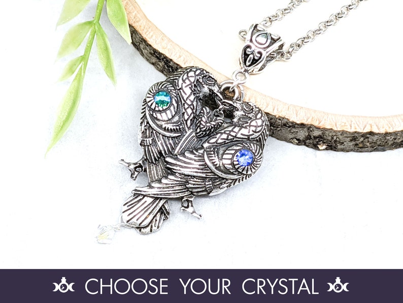 May include: Silver pendant necklace featuring two stylized birds with blue and green crystal accents. The birds are intertwined and have detailed wings and feathers.