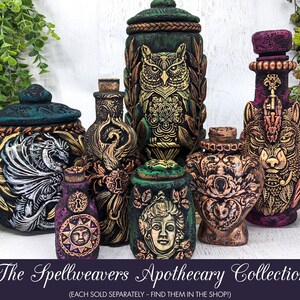 May include: A collection of seven decorative ceramic jars with lids, each featuring a different mythical creature or design. The jars are painted in shades of green, black, gold, and purple, and have intricate details. The jars are labeled "The Spellweavers Apothecary Collection".