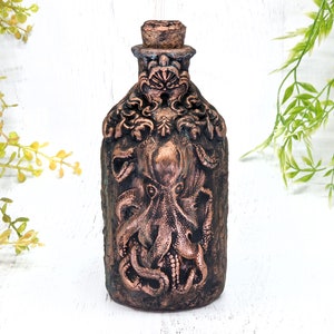 May include: A decorative bottle with a copper finish features an embossed design of an octopus with intricate details. The bottle has a cork stopper and is perfect for adding a unique touch to any home decor.