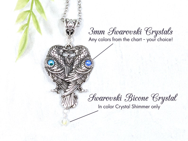 May include: Silver pendant necklace featuring two stylized owls with 3mm Swarovski crystals for eyes. The pendant is attached to a silver chain and has a single Swarovski bicone crystal hanging from the bottom.