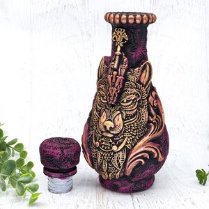 May include: A purple and gold ceramic bottle stopper with a wolf's head design. The stopper has a detailed design with intricate patterns and a gold finish.