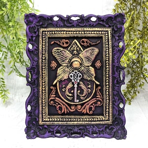May include: A purple ornate frame with gold accents surrounds a black background with a gold butterfly and key design. The butterfly has a large eye in the center and the key has a red jewel.