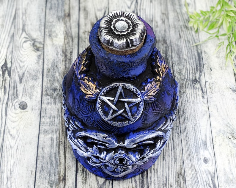 May include: A blue ceramic bottle with a silver pentagram design and a silver flower-shaped stopper. The bottle has gold leaf accents and intricate details.