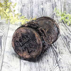 May include: A dark brown ceramic planter with intricate floral designs and the word "Luck" embossed on the bottom.