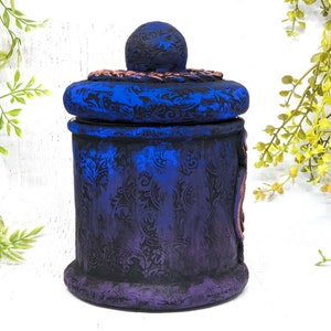 May include: A blue and purple ceramic jar with a decorative lid. The jar has a floral pattern and a distressed finish.