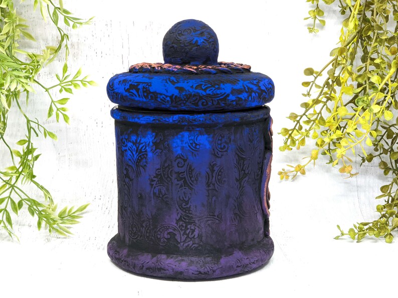 May include: A blue and purple ceramic jar with a decorative lid. The jar has a floral pattern and a distressed finish.
