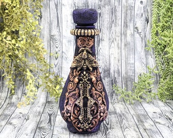 Può includere: Una bottiglia di vetro di colore viola scuro con un design dorato e rame. La bottiglia ha un tappo decorativo e presenta un design a farfalla.