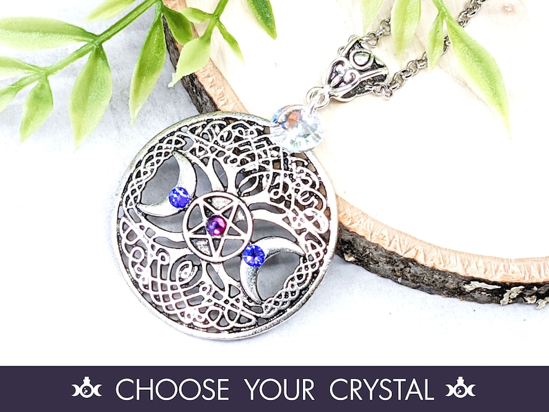 May include: Silver pendant necklace featuring a triple moon design with a pentagram at its centre. The pendant is embellished with blue and purple crystals.