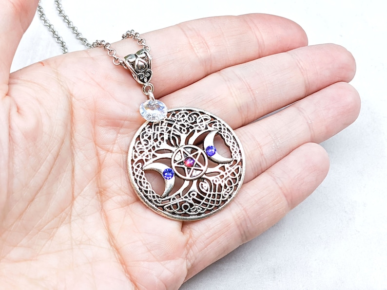 May include: Silver necklace with a circular pendant featuring a triple moon symbol, a pentagram, and three crystals. The pendant is surrounded by a Celtic knot design.