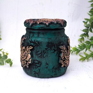 May include: A teal green ceramic jar with a decorative lid. The lid and jar are decorated with gold floral patterns.
