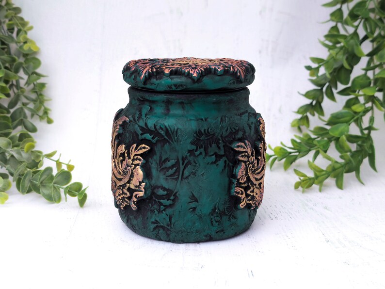 May include: A teal green ceramic jar with a decorative lid. The lid and jar are decorated with gold floral patterns.