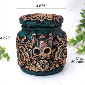 May include: Teal ceramic jar with a gold and copper skull design and a lid. The jar is 4.625 inches tall and 4.875 inches wide. It holds 17 ounces or 30 cubic inches.