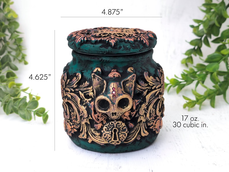 May include: Teal ceramic jar with a gold and copper skull design and a lid. The jar is 4.625 inches tall and 4.875 inches wide. It holds 17 ounces or 30 cubic inches.