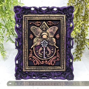 May include: A purple ornate frame with gold accents surrounds a black background with a gold butterfly and key design. The butterfly has a large eye in the center and the key is surrounded by swirling floral details.