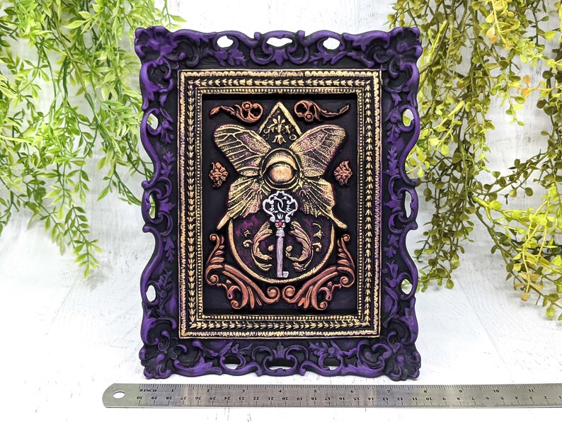 May include: A purple ornate frame with gold accents surrounds a black background with a gold butterfly and key design. The butterfly has a large eye in the center and the key is surrounded by swirling floral details.