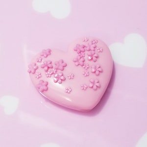 May include: A pink heart-shaped object with small pink flowers embossed on the surface.