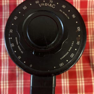 May include: A black Variac dial with white markings and a central knob. The dial has numbers from 0 to 130, with the text "VARIAC" and "GENERAL RADIO CO." visible. The dial is connected to a black plug.