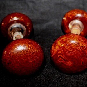 May include: A set of four round door knobs featuring a glossy, marbled finish in shades of deep reddish-brown and amber. Each knob has a smooth, spherical surface with a metallic base attachment visible on the two knobs positioned in the back.