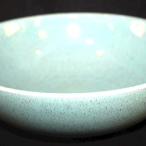 May include: A light blue ceramic bowl with a speckled texture. The bowl has a wide, shallow design and a smooth interior. The bowl is likely used for serving food or as a decorative piece.