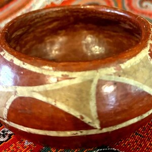 May include: A handcrafted, round, brown ceramic bowl with a glossy finish. The bowl features a geometric design in cream and white, adding a decorative touch. The bowl is likely used for serving or display.