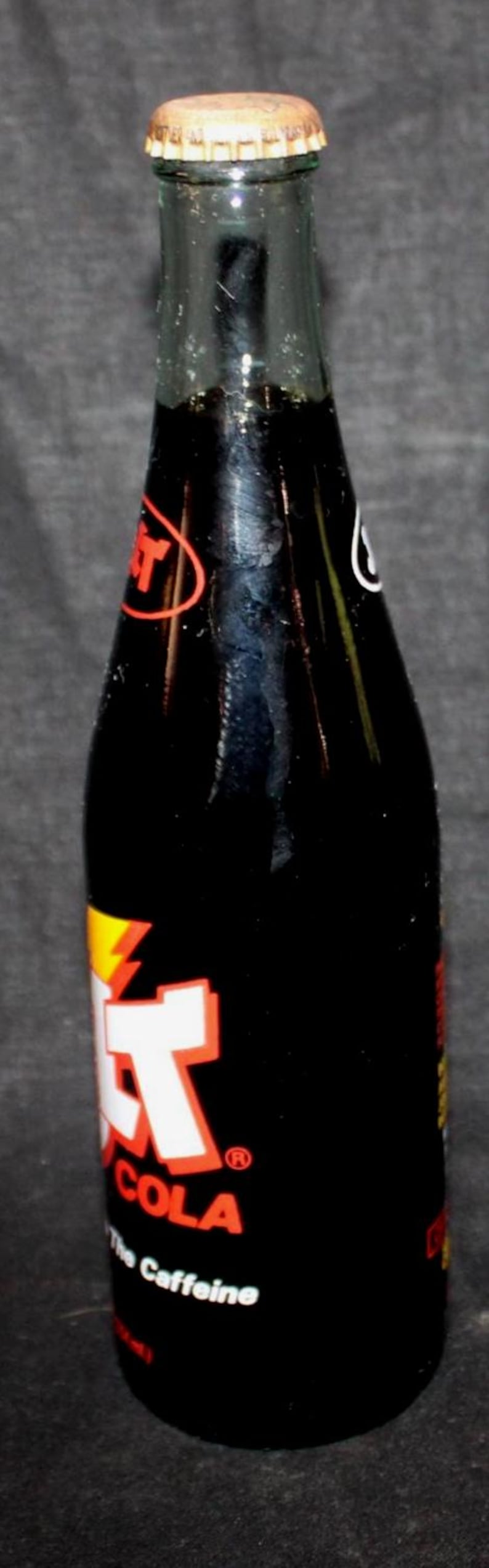 May include: A vintage glass bottle of Jolt Cola, a caffeinated soft drink. The bottle is mostly black with red, white, and yellow branding. The bottle cap is gold-colored.