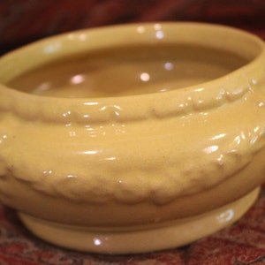 May include: A yellow ceramic bowl with a decorative, scalloped rim. The bowl has a glossy finish and is perfect for serving or displaying.