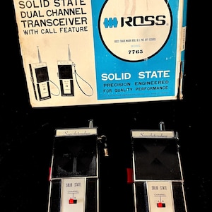 May include: A pair of black and silver Ross solid state dual channel transceivers with antennas and wrist straps, accompanied by their original white and blue cardboard box featuring the text Superheterodyne, Model 7765, and Ross Electronics.
