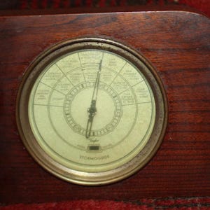 May include: A vintage wooden barometer with a brass face and a needle pointing to "Stormy". The face is labeled with different weather conditions.