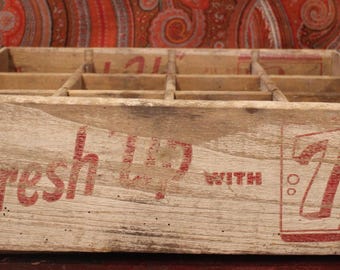 Op de afbeelding: Vintage houten 7 Up frisdrankkrat met rode letters en afbeeldingen. De krat is verdeeld in compartimenten en versterkt met metalen randen. De woorden "Fresh Up With 7 Up" zijn zichtbaar.