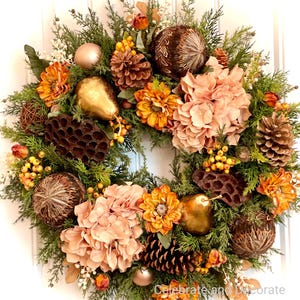 May include: A decorative wreath featuring a mix of faux greenery, orange and peach-colored flowers, pinecones, and gold pear ornaments. The wreath is adorned with small gold-colored spheres and brown decorative balls, creating a festive autumn theme.