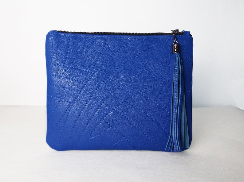 May include: A bright blue clutch bag with a stitched geometric design. It has a black zip and a matching blue tassel. This accessory is ideal for carrying essentials, a fashionable item.