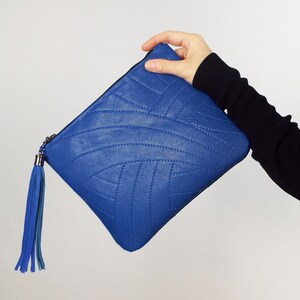 May include: A bright blue clutch bag with a quilted design. It has a matching blue tassel and a silver zip pull. The bag is set against a white backdrop.