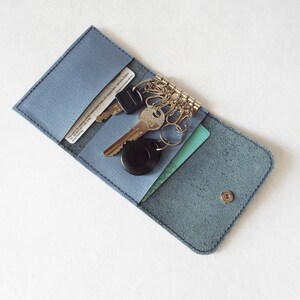 May include: A blue leather key holder with a snap closure. The holder has two slots for cards and a key ring with multiple keys.