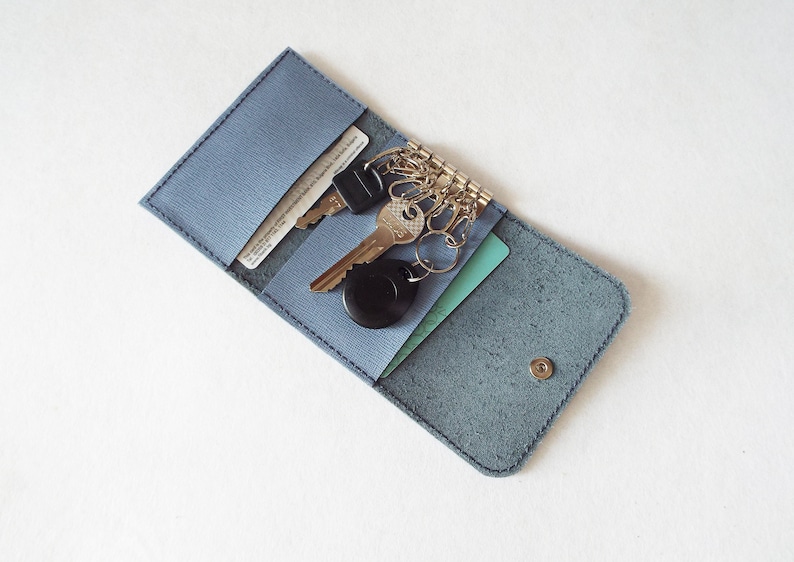 May include: A blue leather key holder with a snap closure. The holder has two slots for cards and a key ring with multiple keys.