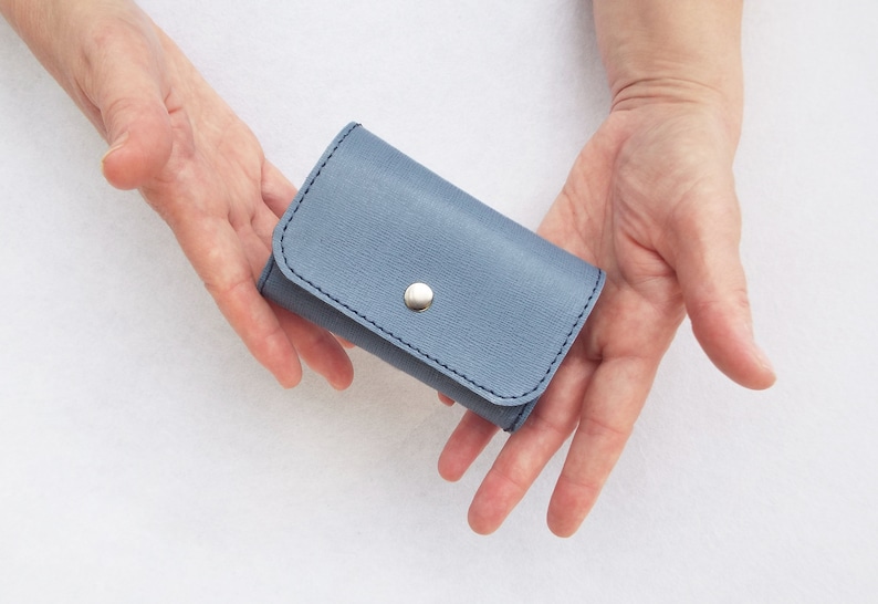 May include: A small, light blue leather wallet with a silver button closure.