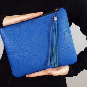 May include: A bright blue clutch bag with a stitched geometric design. It has a zip closure and a long, teal tassel. The bag is displayed against a plain background.