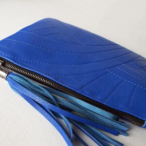 May include: A bright blue clutch bag with a quilted pattern and a black zip. It has a tassel made of blue leather strips. A fashionable accessory.