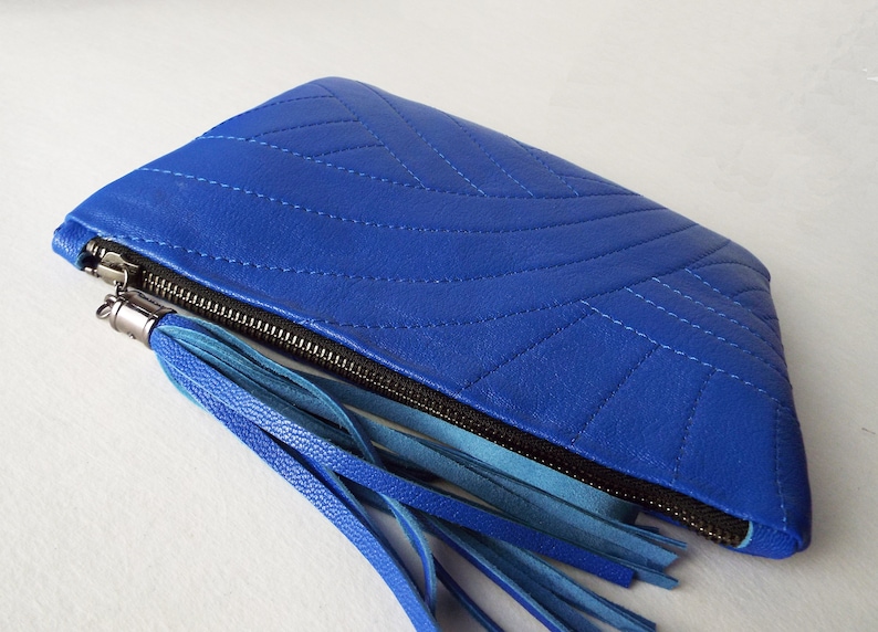 May include: A bright blue clutch bag with a quilted pattern and a black zip. It has a tassel made of blue leather strips. A fashionable accessory.
