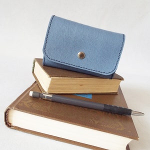 May include: A stack of three books with a blue leather wallet on top. A pencil is lying on top of the books.
