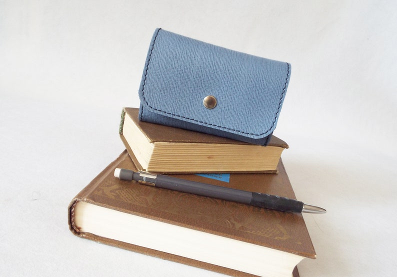 May include: A stack of three books with a blue leather wallet on top. A pencil is lying on top of the books.