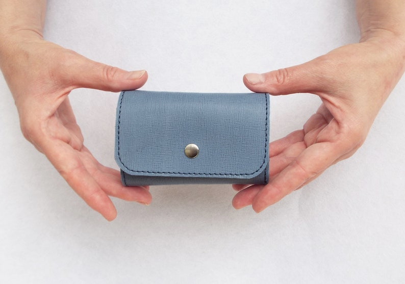 May include: A small, light blue leather wallet with a silver button closure.