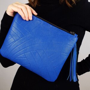May include: A bright blue clutch bag with a stitched geometric design. It has a black zip and a blue tassel. This fashionable accessory is ideal for carrying essentials, a stylish addition.
