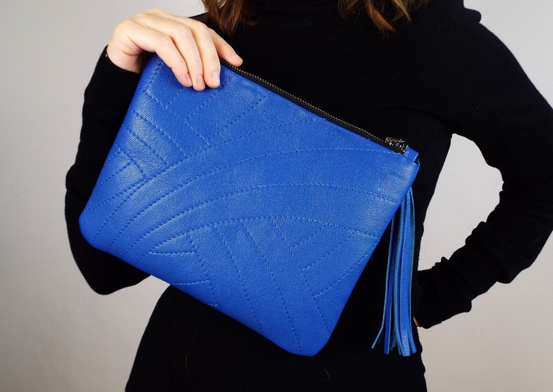 May include: A bright blue clutch bag with a stitched geometric design. It has a black zip and a blue tassel. This fashionable accessory is ideal for carrying essentials, a stylish addition.
