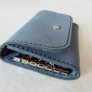 May include: A blue leather key holder with a metal key ring. The key holder has a flap that closes with a snap.